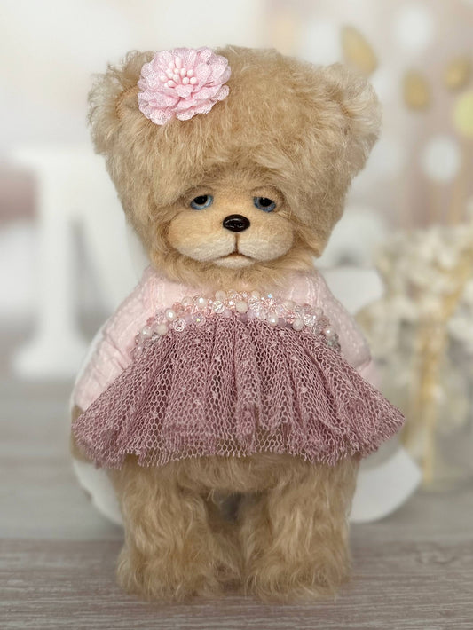 Teddy bear wearing a pink dress with a flower on its head against a blurred background
