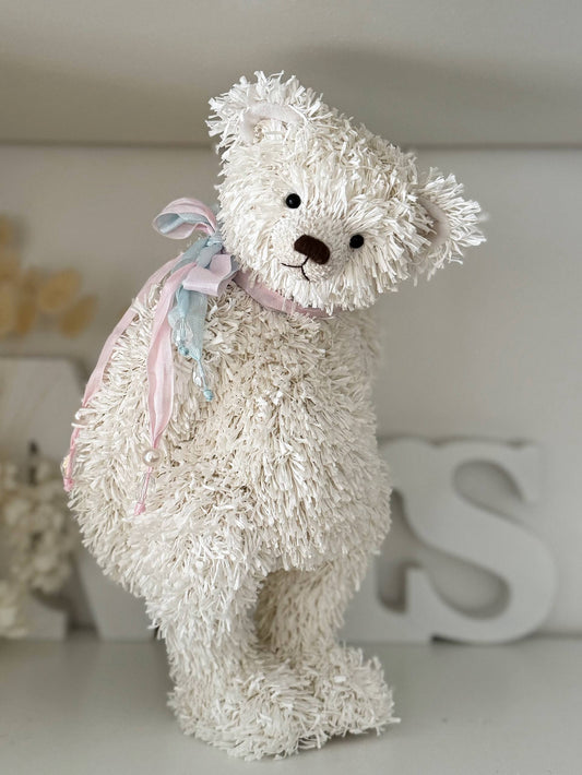 White teddy bear with a pink bow on a white surface